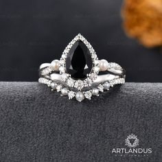 a black and white diamond ring on top of a gray cloth with pearls around it