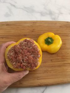 a person is holding a stuffed pepper on a cutting board next to a bell pepper