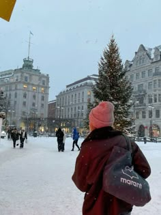 a person standing in front of a christmas tree on a city street covered in snow