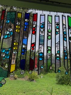 several colorful stained glass pieces hanging from a window sill in front of a grassy field