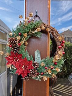 a christmas wreath hanging on the side of a door with pine cones and poinsettis