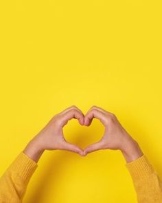 two hands in the shape of a heart on a bright yellow background with copy - up space