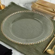 an empty plate on a green placemat next to gold utensils