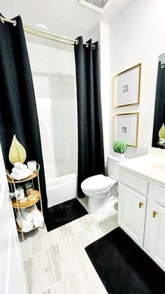 a white bathroom with black shower curtains and gold accents on the wall above the toilet