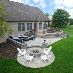 an outdoor patio with seating and fire pit in the middle of it, surrounded by green grass