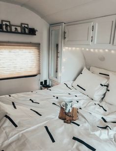 a bed with white sheets and pillows in a room that has lights on the headboard