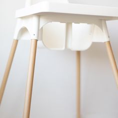 a close up of a white chair with wooden legs and an object in the background