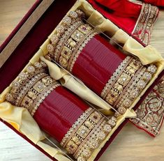 two red and gold bracelets in a box on a wooden table with other jewelry