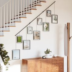 a wooden dresser sitting under a stair case next to a wall with pictures on it