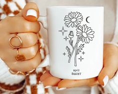 a woman holding a coffee mug with daisies on the front and side in her hands