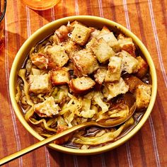 a yellow bowl filled with noodles and tofu on top of a table next to a glass of orange juice