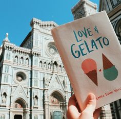 someone holding up a book about love and gelato in front of a building with an ice cream cone on it