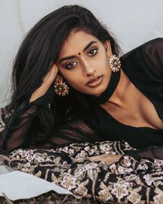 a woman laying on top of a bed next to a white wall and wearing earrings