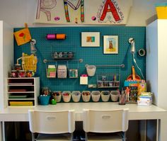 there is a desk with two white chairs and several storage bins on the wall