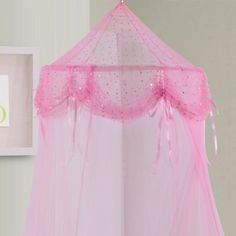 a pink mosquito net hanging from the ceiling next to a white wall with framed pictures on it