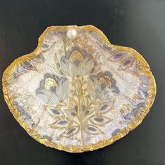 a decorative dish with gold trimmings and blue flowers on the bottom, sitting on a black surface