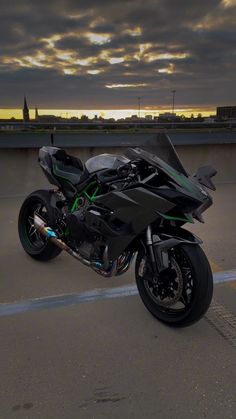 a black motorcycle parked on top of a parking lot next to a bridge at sunset