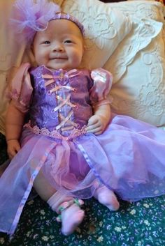 a baby doll wearing a purple dress sitting on a bed