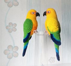 two crocheted parrots sitting on top of each other in front of a wall