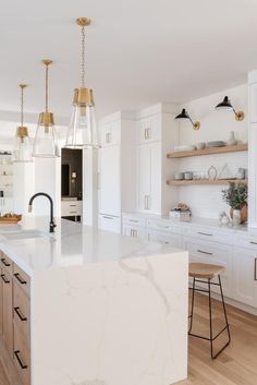 a large kitchen with white cabinets and marble counter tops, along with hanging lights above the island