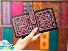 a hand holding an open wallet in front of colorful art work on the wall behind it