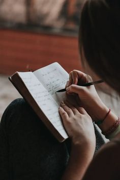 a woman writing on a notepad with a pen in her hand while sitting down