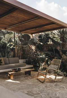 a living room filled with furniture next to a stone wall covered in plants and trees