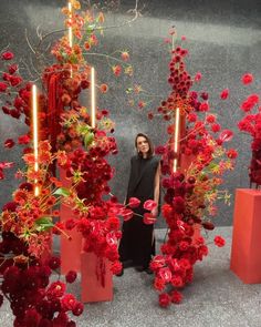 a woman standing between two tall red vases with flowers on them and candles in the background