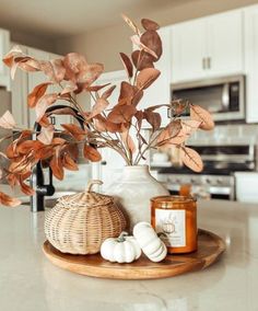 a white vase filled with lots of leaves on top of a counter next to a candle