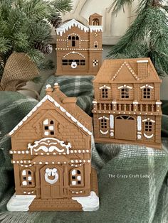 three gingerbread houses sitting on top of a bed next to christmas tree branches and pine cones