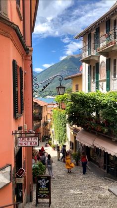 people are walking down an alley way in the mountainside town with shops and restaurants