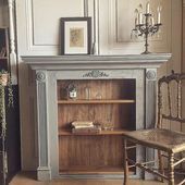 a room with a chair, book shelf and pictures on the wall