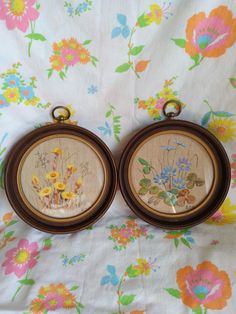 two framed pictures with flowers on them sitting on a floral print cloth covered tablecloth