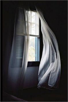 an open window in a dark room with sheer curtains