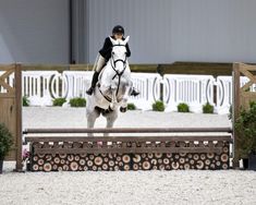 a woman riding on the back of a white horse jumping over an obstacle in front of a building