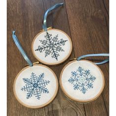 three cross - stitch snowflakes hanging from wooden hoops on a wood floor