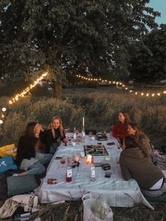 four women sitting at a picnic table with drinks and snacks on it in the evening