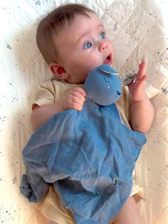 a baby laying on top of a bed with a stuffed animal in it's mouth