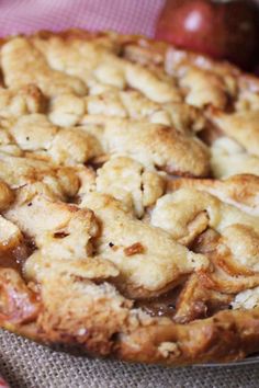 an apple pie on a table with apples in the background