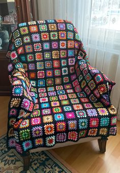 a crocheted granny blanket sitting on top of a chair in front of a window