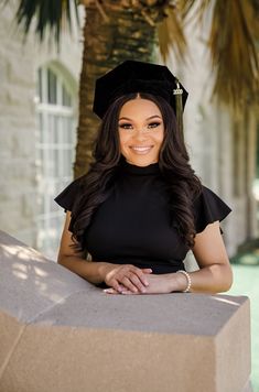 a woman wearing a graduation cap and gown posing for a photo in front of a palm tree