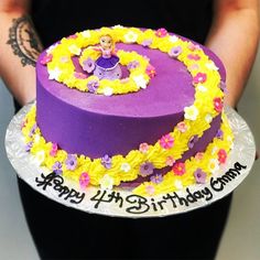 a person holding a purple and yellow birthday cake