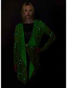 a woman standing in front of a black background wearing a green cardigan with lights on it