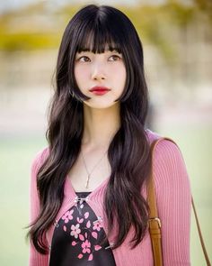 a woman with long black hair wearing a pink sweater and carrying a brown purse in her hand