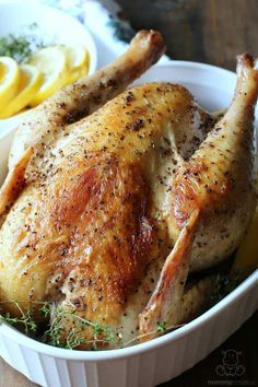 a roasted chicken in a white dish with lemons and herbs