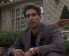 a man sitting on the ground in front of a house with his hand on his knee