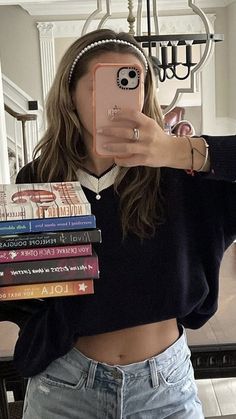 a woman taking a selfie with her cell phone and stack of books in front of her