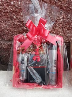 the gift basket is wrapped in plastic and has pink ribbon around it, along with two bottles of deodorant