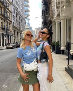 two women standing next to each other in the street with headphones on their ears