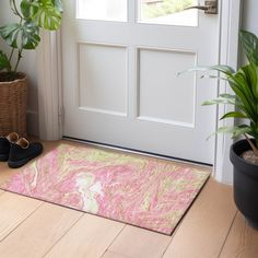 a pink and green door mat sitting on top of a wooden floor next to a potted plant